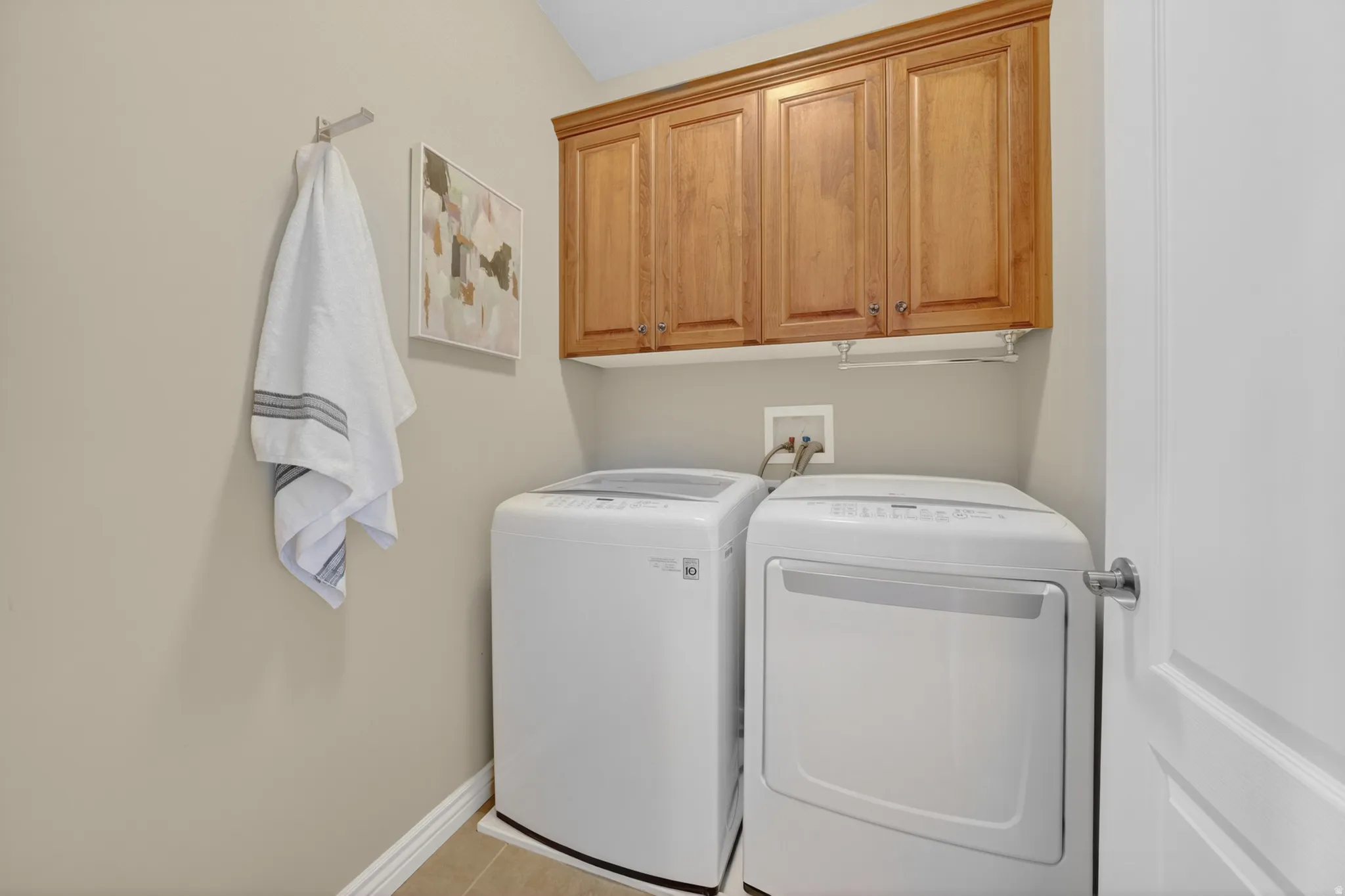 Laundry area featuring wood cabinetry, light beige wall paint, white baseboards, and tiled flooring