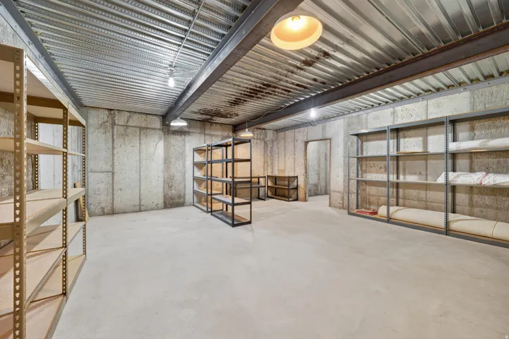 Spacious basement  storage room featuring concrete walls, a concrete floor, and exposed metal beam ceiling