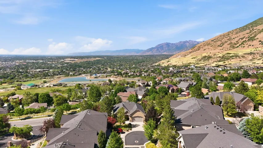 Aerial perspective showcasing a residential area with varied rooflines and abundant mature trees, set against a backdrop of mountains and valley