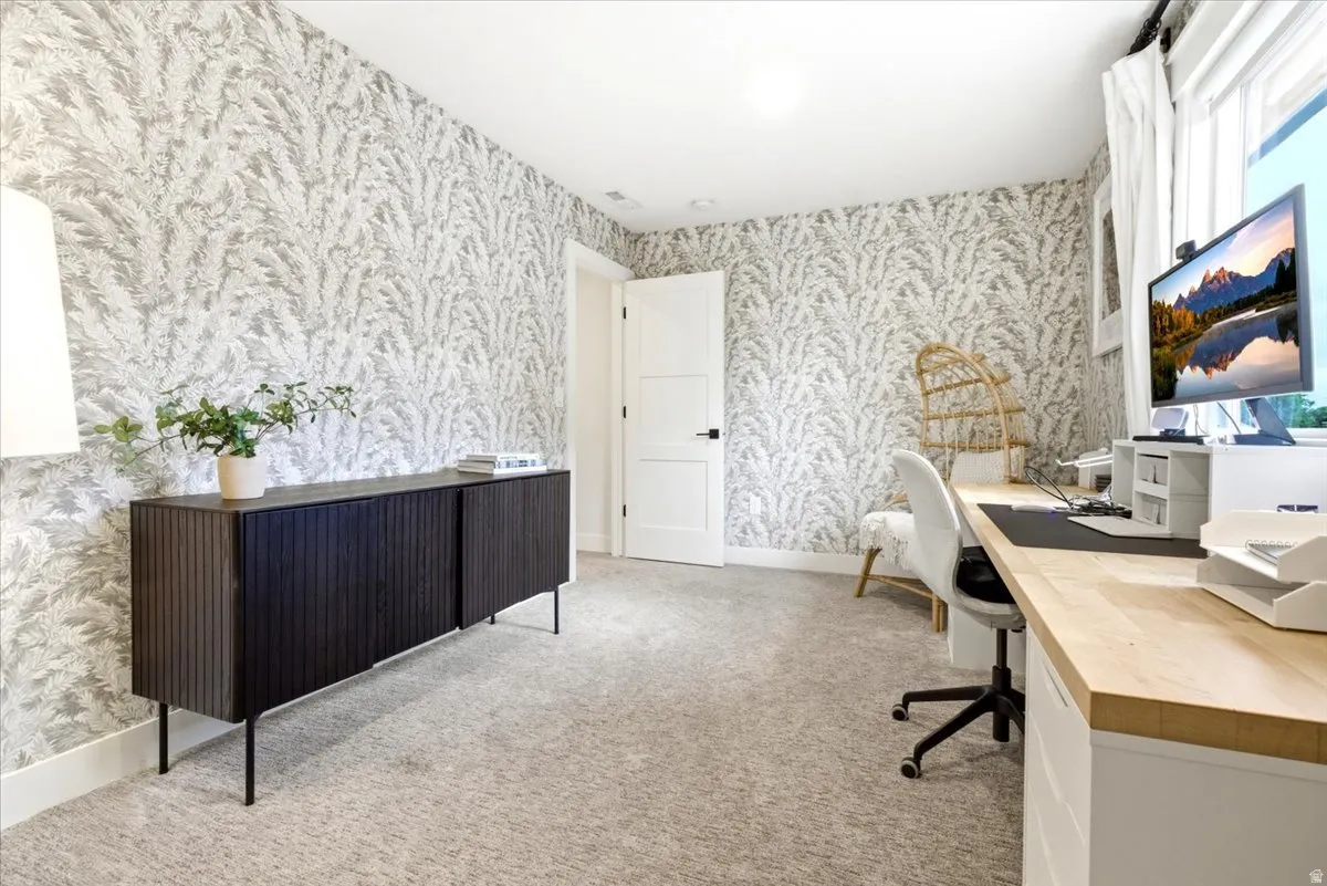 Room featuring patterned wall covering, neutral carpet flooring, and a window with white drapes