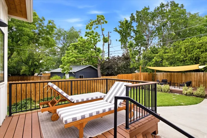 Expansive wood-finish deck with black metal railings, leading to a landscaped lawn