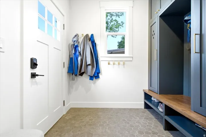 Entryway featuring hexagonal floor tiles, white paneled door with matte black hardware, built-in storage lockers in a deep blue finish, and a wood-finish bench with open shelving
