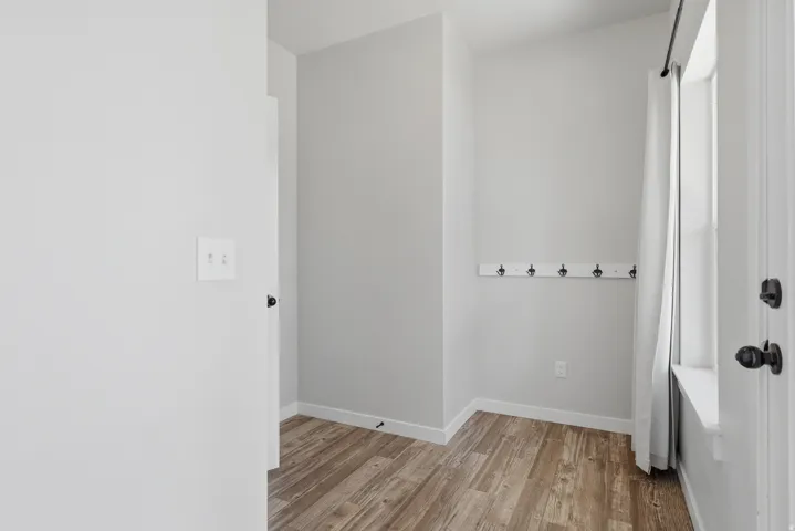 Entryway mudroom area featuring wood-finish flooring, light grey painted walls, white baseboards, and a built-in wall-mounted coat rack