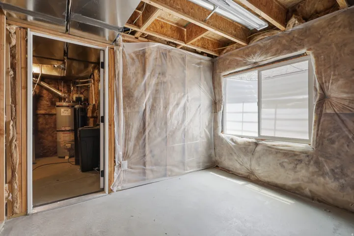 Unfinished basement room with exposed wood framing, insulation, and a single window with white trim