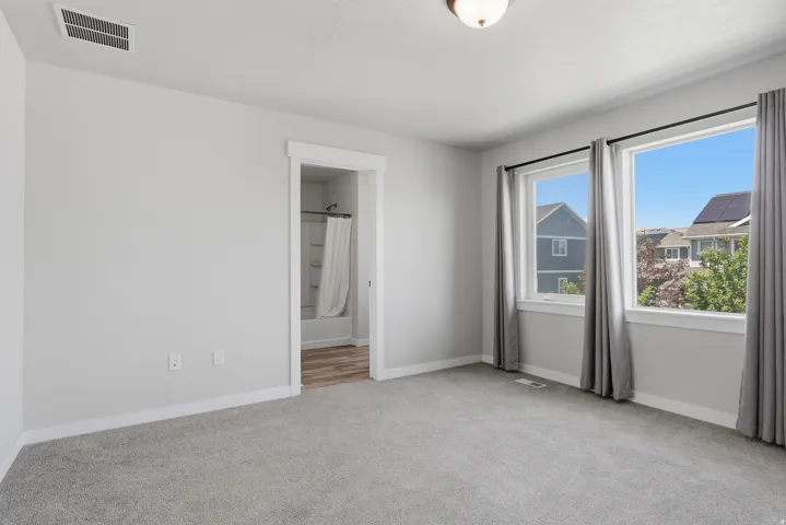 Carpeted room with light gray walls, featuring two large windows with gray drapes and white trim
