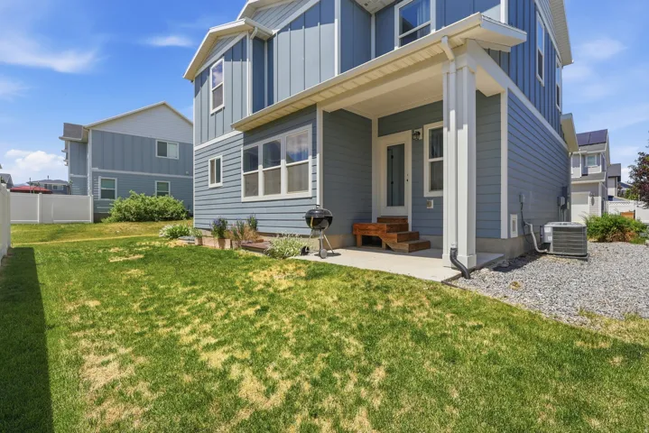 Expansive grassy backyard featuring a concrete patio, exterior wood steps, covered porch, and white vinyl fencing