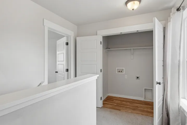Dedicated laundry closet featuring wood-finish flooring, overhead shelving, and utility hookups
