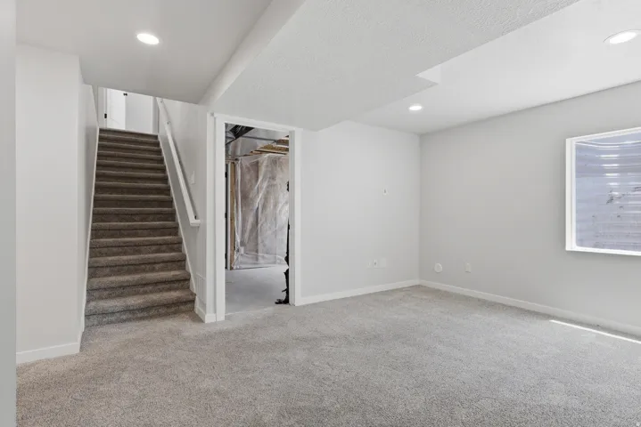 Finished interior space featuring light gray carpeting, recessed lighting, and a window with horizontal blinds