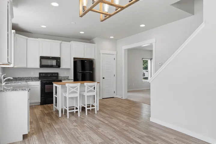 Kitchen featuring white cabinetry, black appliances, speckled countertops, and wood-finish flooring