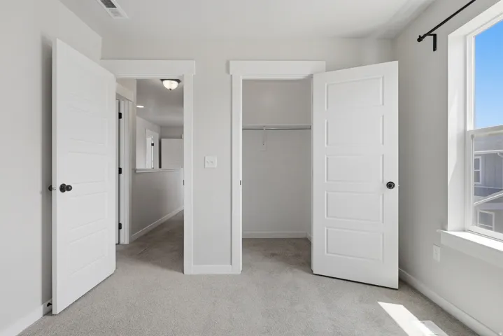 Carpeted room featuring a window with a black curtain rod, white five-panel interior doors with black hardware, and a closet with a built-in wire shelf and hanging rod