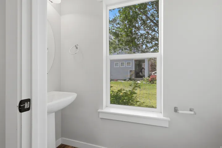 Pedestal sink with a circular mirror and overhead lighting