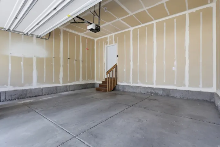 Spacious garage featuring a concrete floor, automatic garage door opener, and interior access door with wooden steps