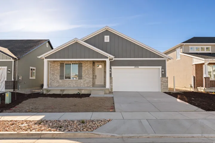 Contemporary ranch-style residence featuring a prominent two-car garage, gray vertical siding, light-toned stone accents, a covered entry porch, and a concrete driveway