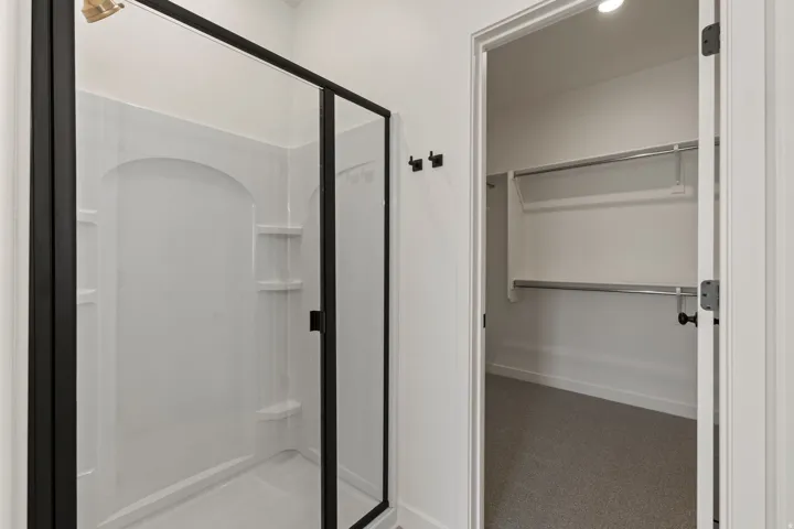 Walk-in shower with black-framed glass enclosure, integrated shelving, and a brass-finish showerhead