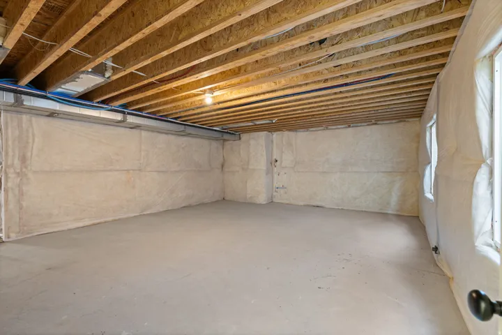 Unfinished basement with exposed wood-finish ceiling joists, concrete flooring, and insulated walls