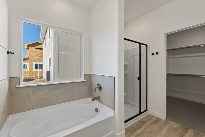 Bathroom featuring a white soaking tub, light gray tile wainscoting, and a window with a white frame