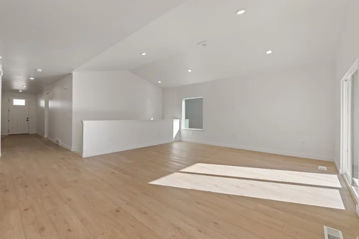 Open-concept living area featuring light wood-finish flooring, recessed lighting, and vaulted ceilings