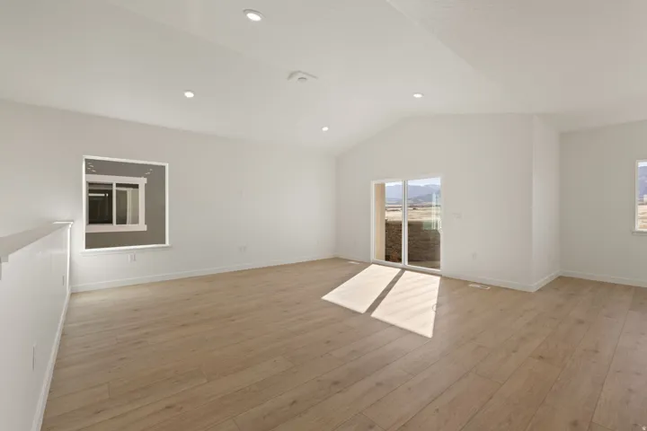 Spacious room featuring wood-finish flooring, vaulted ceilings, and recessed lighting