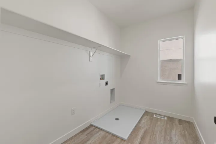 Utility room featuring a window, built-in shelving, wood-finish flooring, and a floor drain