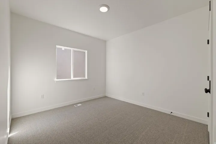 Bright interior space featuring a window with white trim, recessed ceiling lighting, textured carpet flooring, and white baseboards