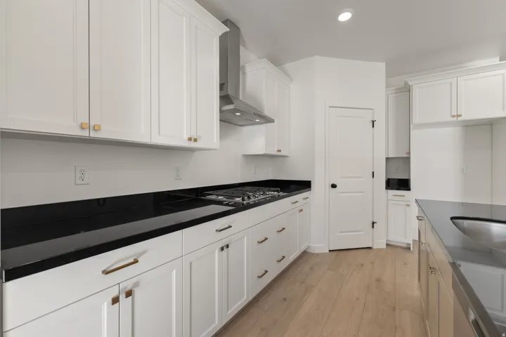 Modern kitchen featuring white shaker cabinetry, dark countertops, and wood-finish flooring