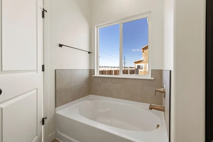 Soaking tub with a tiled surround, bronze-finish fixtures, and a dual-pane window
