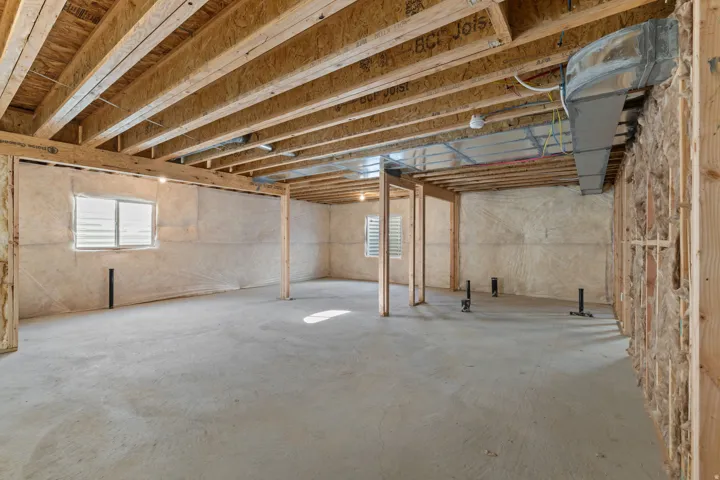 Unfinished basement space featuring exposed wood joists, concrete flooring, two windows with blinds, exposed ductwork, and partial framing