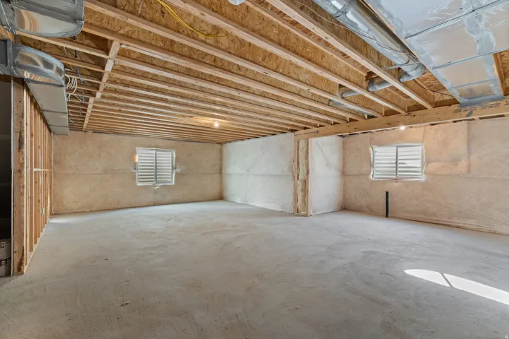 Unfinished basement featuring exposed wood joists, concrete flooring, two windows with louvered covers, and visible ductwork