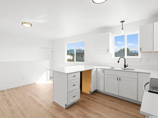 Kitchen featuring white shaker cabinetry, light-toned wood-finish flooring, white countertops, and a black gooseneck faucet