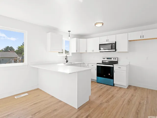 Modern kitchen featuring white cabinetry, light countertops, wood-finish flooring, a built-in microwave, and a contemporary range