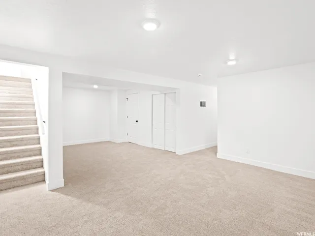 Spacious carpeted room featuring white walls and trim, recessed lighting, and a staircase with a white railing