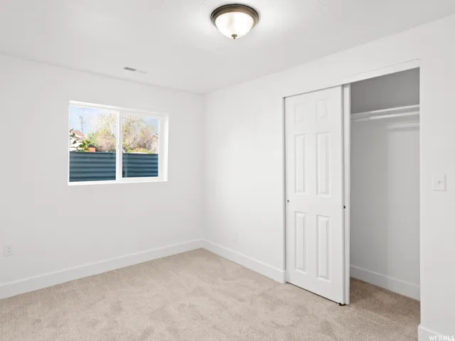 Carpeted room featuring a white-framed window, bright white walls, baseboard trim, a built-in closet with sliding six-panel doors, and a ceiling-mounted light fixture