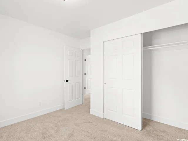 Neutral wall color with plush carpeting, featuring a multi-panel sliding closet door and a six-panel interior door with dark hardware