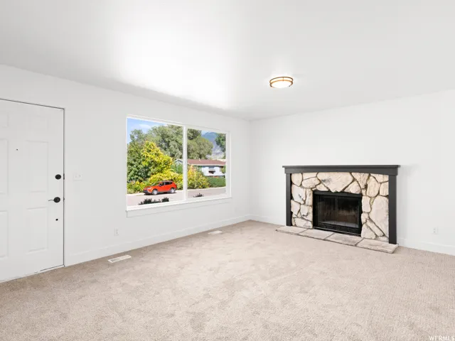 Cozy living area featuring a stone-clad fireplace with a dark mantel, neutral carpeting, a large window, and a paneled entry door