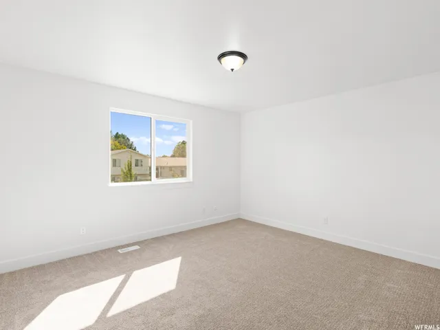 Room featuring light tan carpet flooring, white walls, a white window frame, and a flush-mount ceiling light fixture