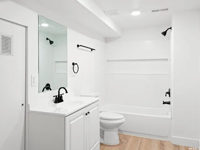Bathroom featuring a white vanity with integrated sink, matte black fixtures, full-size mirror, white tub with shower, and wood-finish flooring