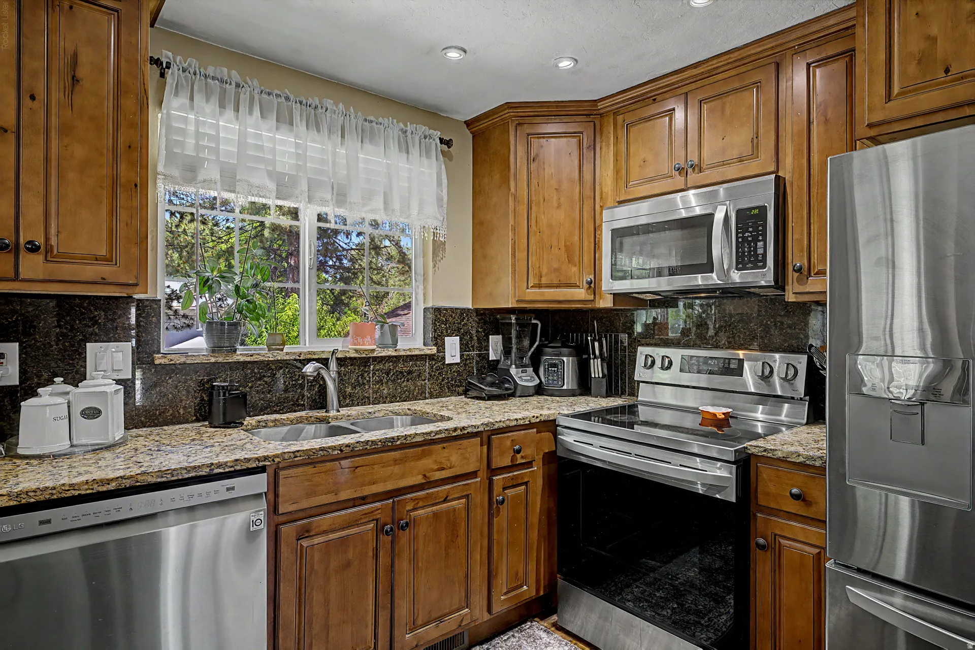 Kitchen featuring stainless steel appliances, granite countertops, wood cabinetry, and a double basin sink