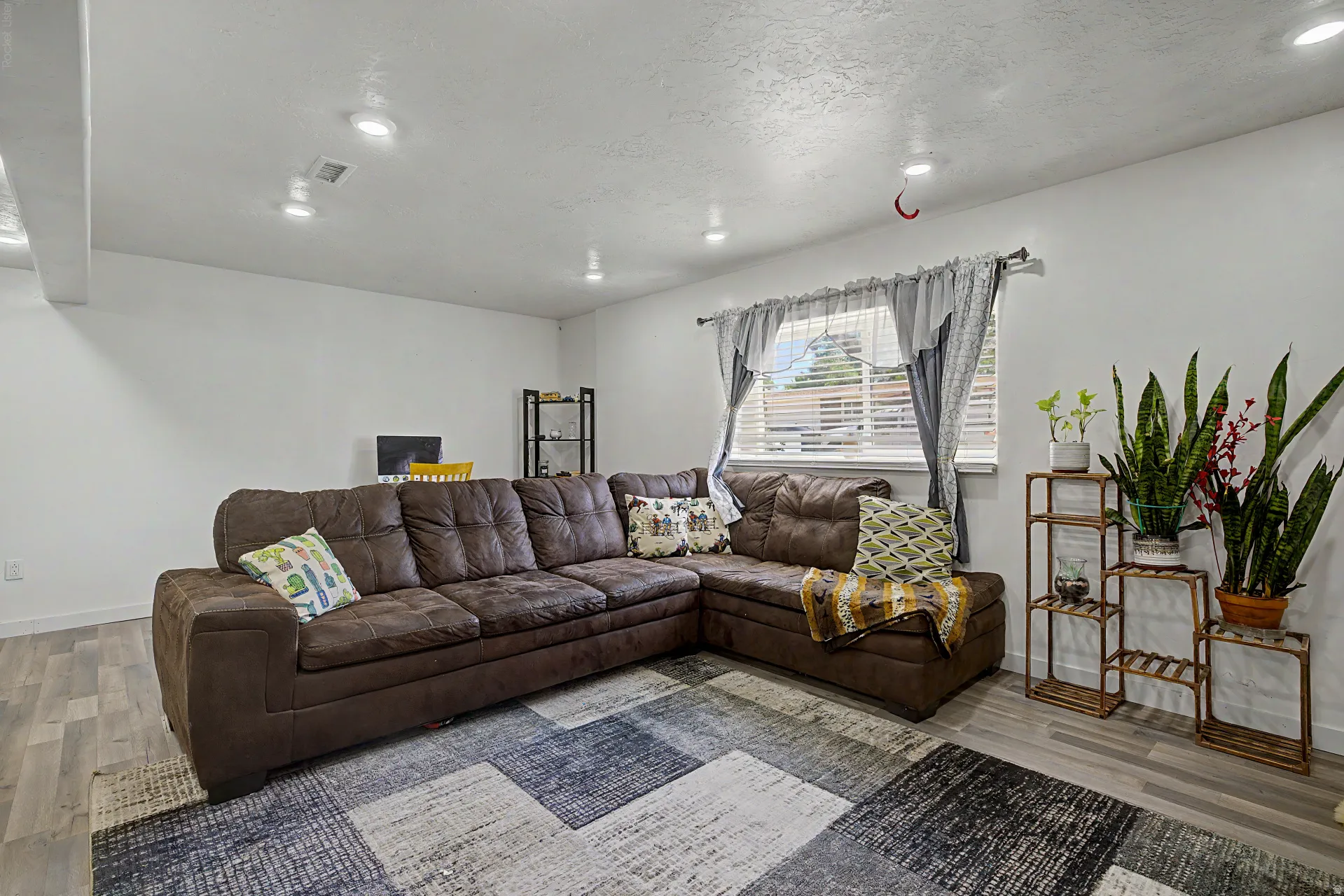 Spacious living area featuring light wood-finish flooring, recessed lighting, and a large window with blinds