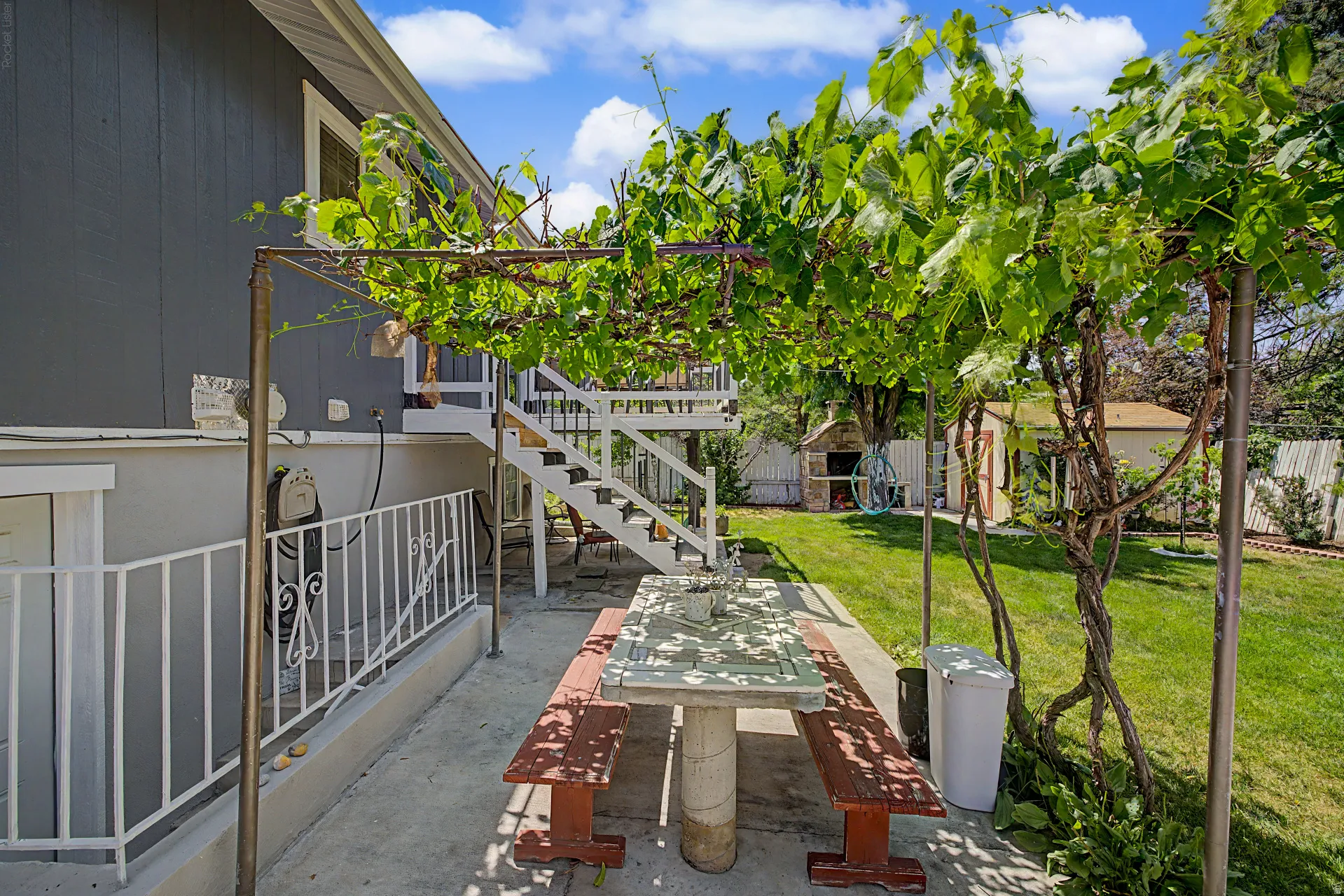 Outdoor patio featuring a concrete surface, overhead trellis with abundant foliage, and a detached storage shed