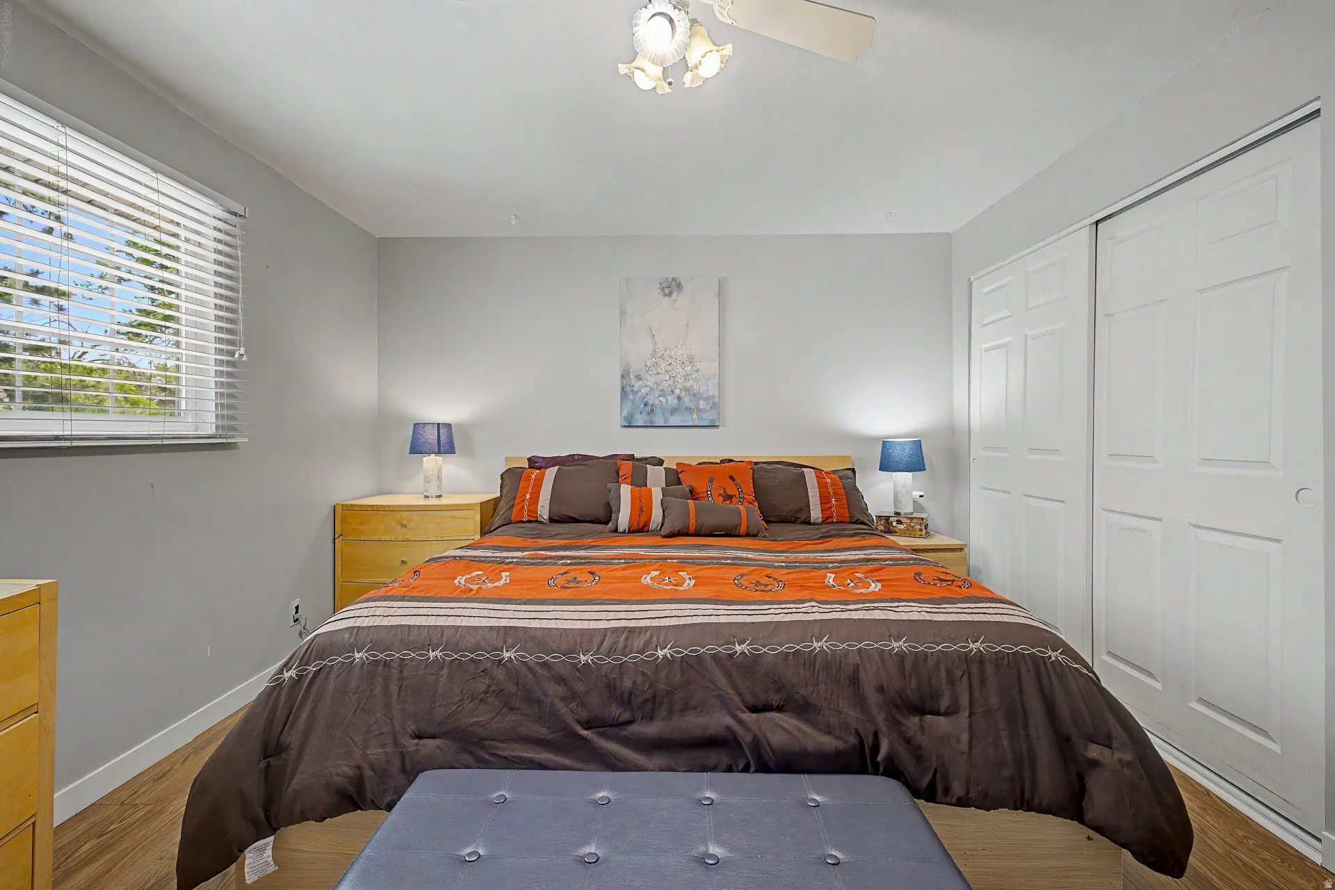 Room featuring wood-finish flooring, a window with horizontal blinds, and a built-in closet with bifold doors