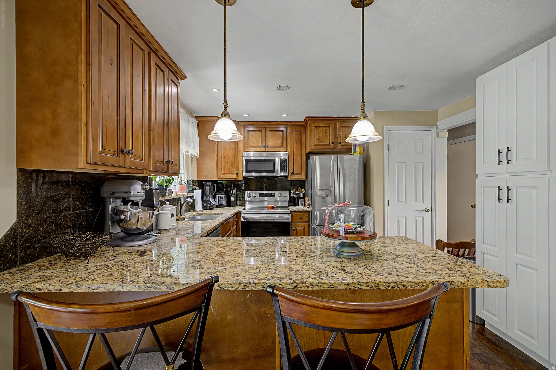 Kitchen showcasing a spacious island with granite countertops, wood-finish cabinetry, stainless steel appliances, and pendant lighting