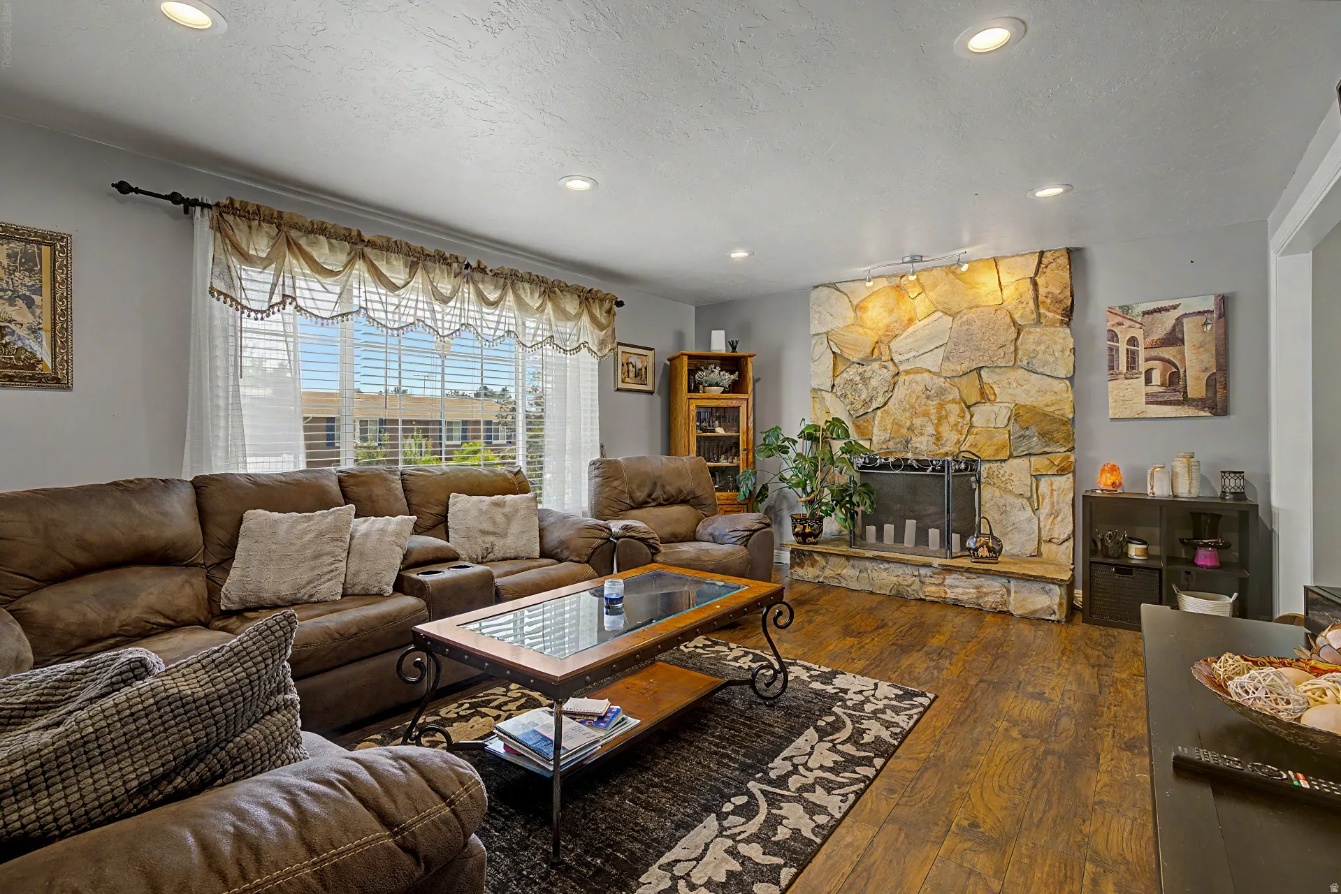Living area featuring a floor-to-ceiling stone fireplace, recessed lighting, wood-finish flooring, and a large window with horizontal blinds