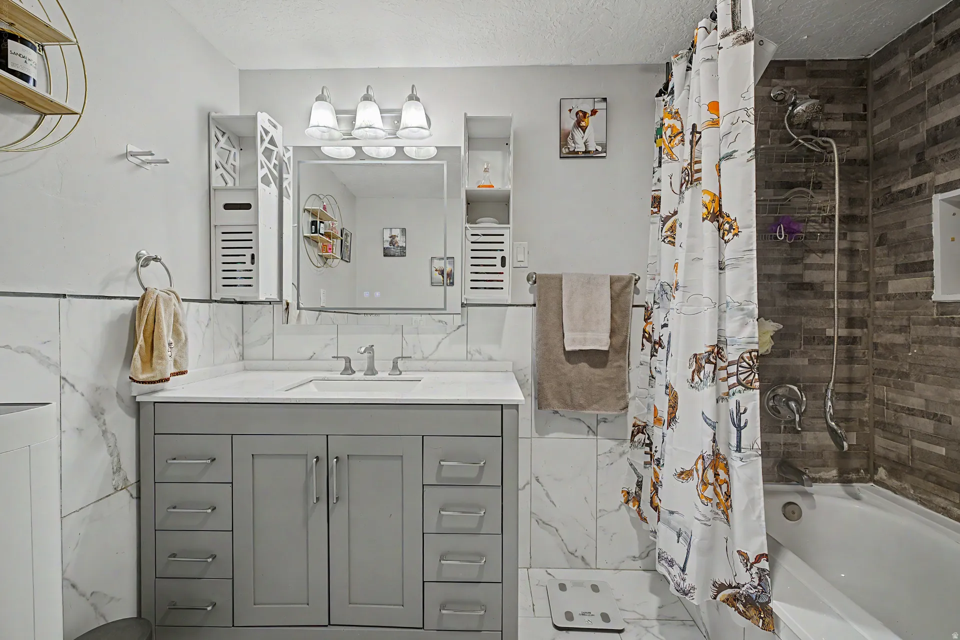 Bathroom featuring a gray vanity with an integrated sink, a large wall-mounted mirror, and a three-light fixture