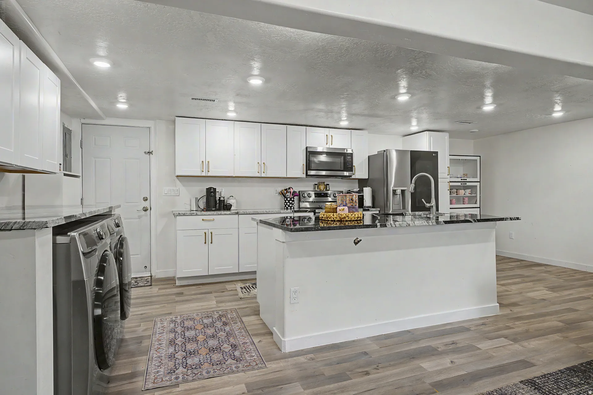 Open-concept kitchen featuring white cabinetry, black stone countertops, stainless steel appliances, a center island with bar seating, and wood-finish flooring
