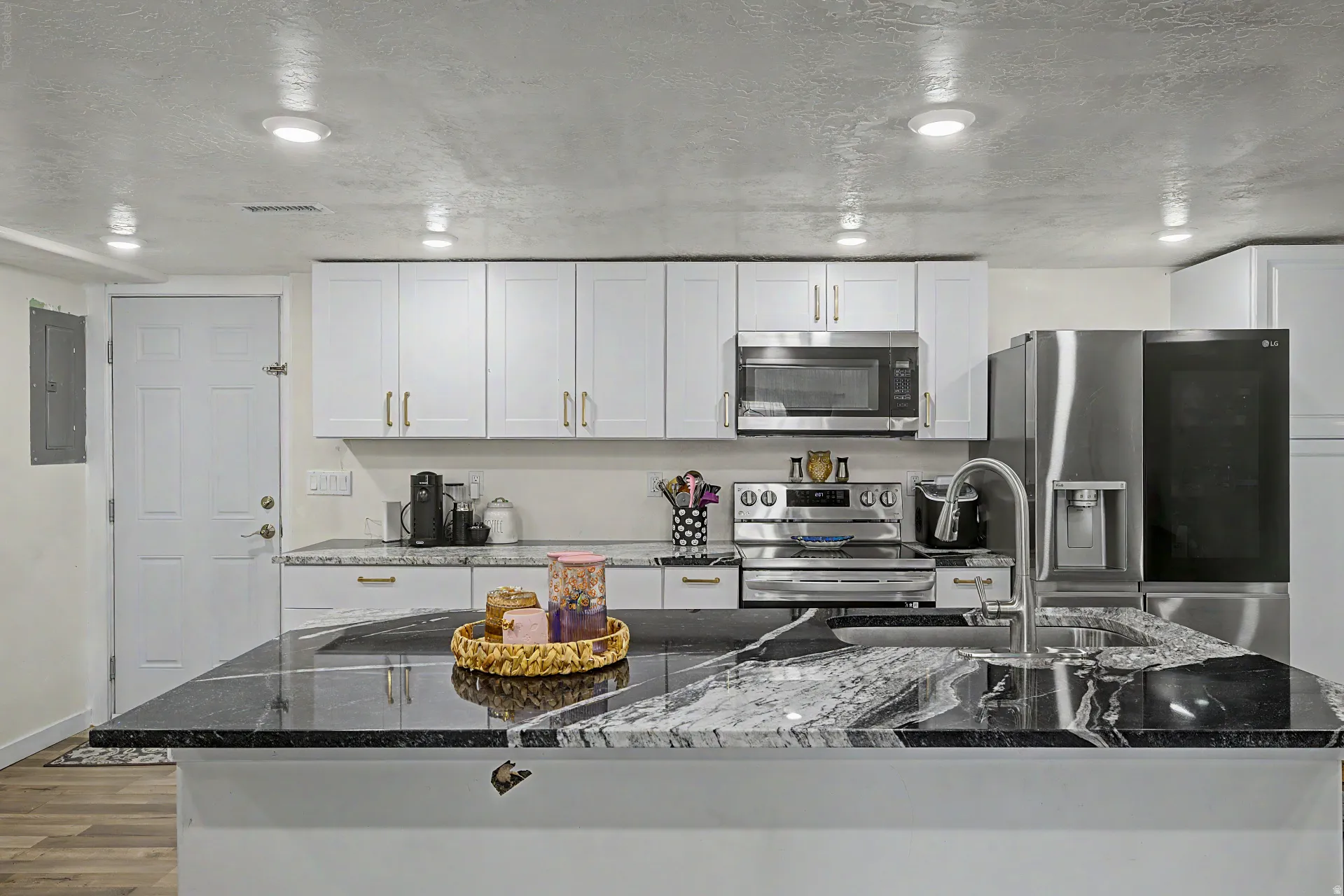 Kitchen featuring a large island with a black and white variegated countertop, white cabinetry with gold-tone hardware, stainless steel appliances, and recessed lighting