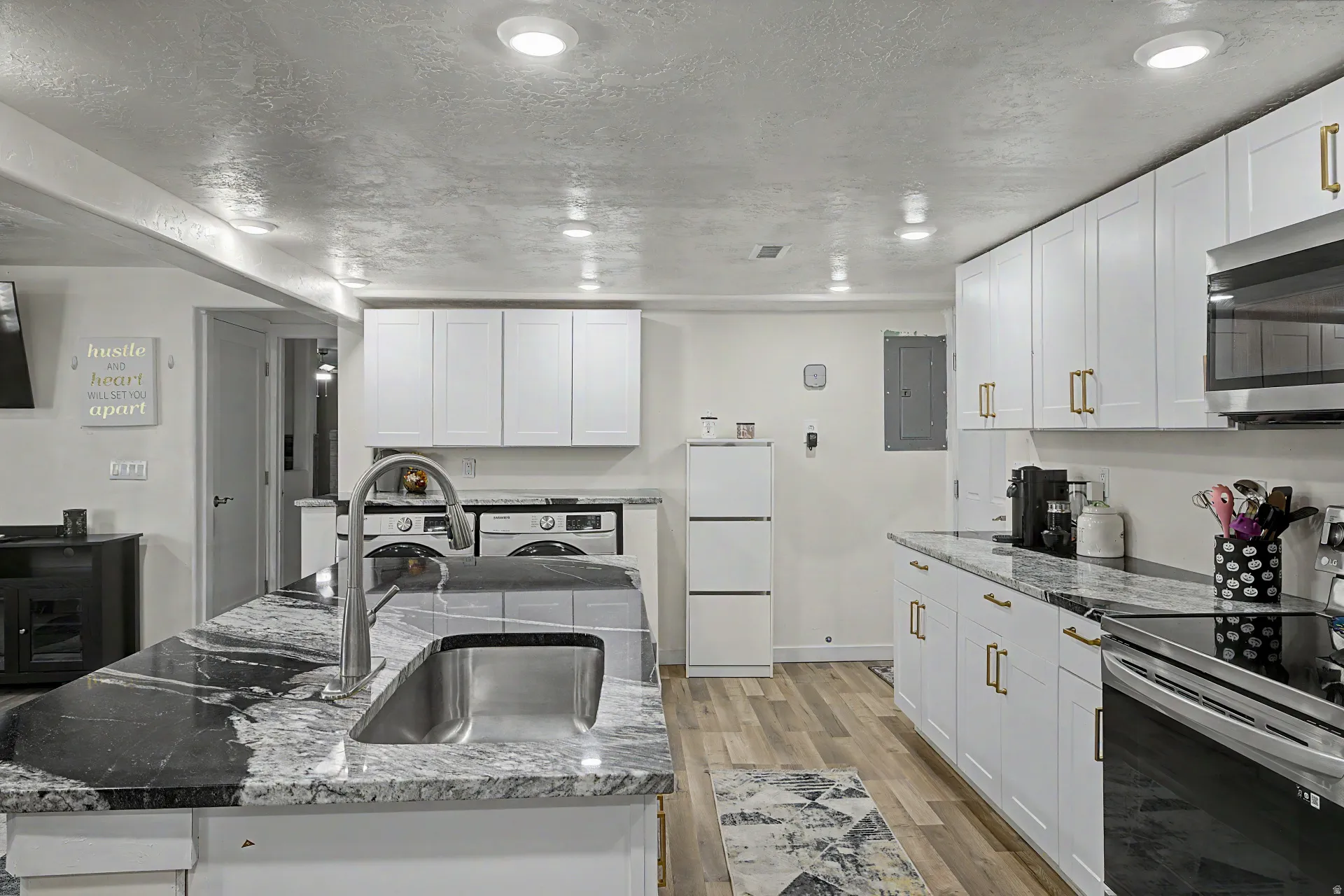 Kitchen featuring an island with a stainless steel sink, wood-finish flooring, white cabinetry with gold-tone hardware, a stainless steel range, and a built-in microwave