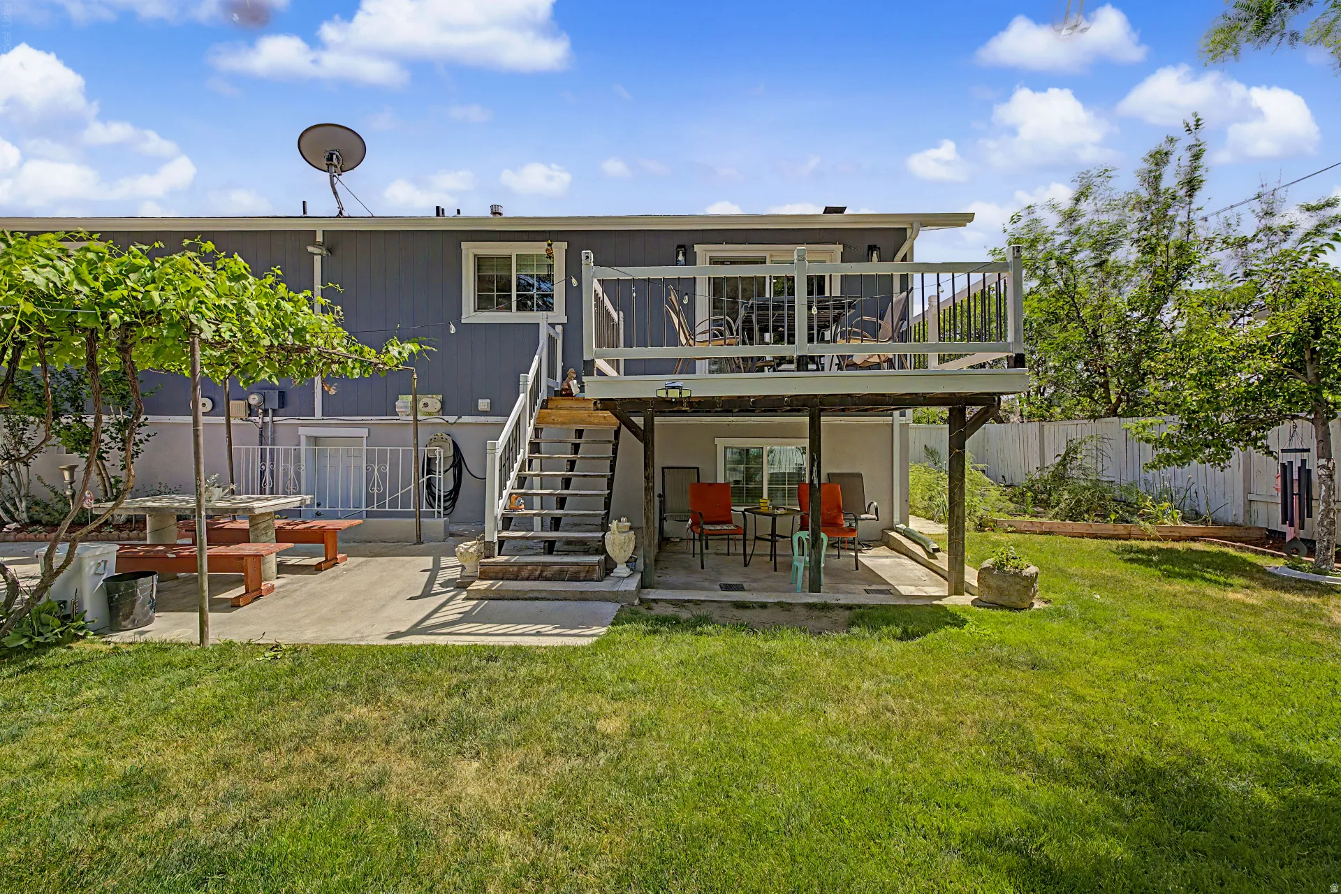 Multi-level backyard featuring a spacious upper deck with white railings, a lower-level concrete patio, and an additional concrete patio with a permanent stone picnic table