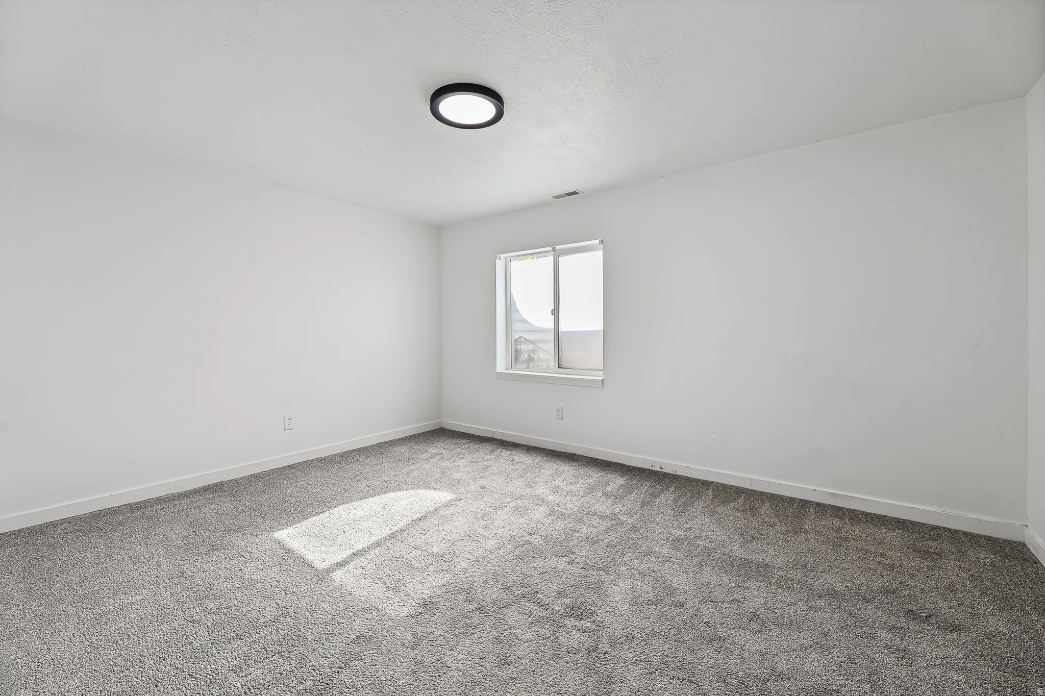 Spacious room featuring neutral carpeting, white walls, and a modern ceiling light fixture