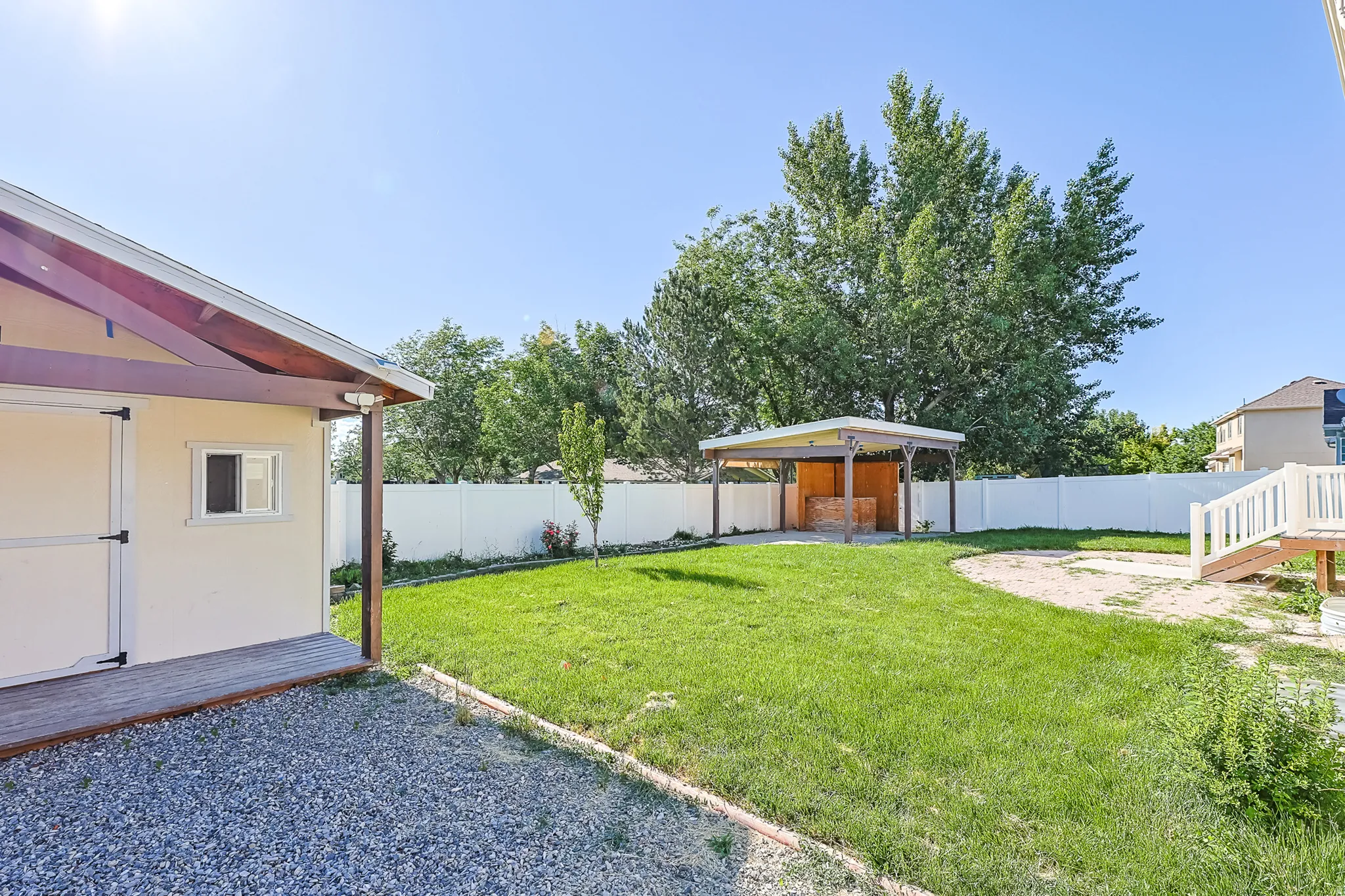 Expansive backyard featuring a lush lawn, gravel path, a covered patio structure, and a dedicated sand area