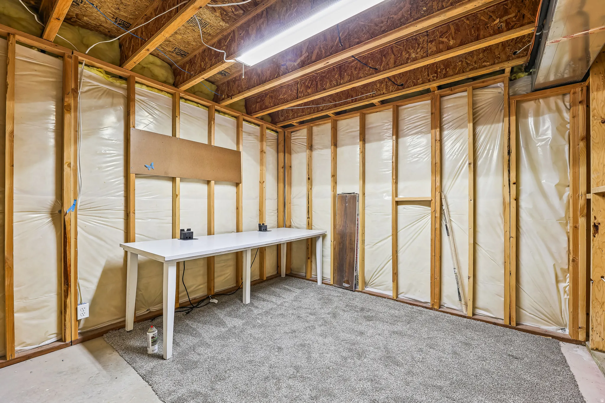 Unfinished basement area featuring exposed wood framing, ceiling joists, and a partial gray carpet installation